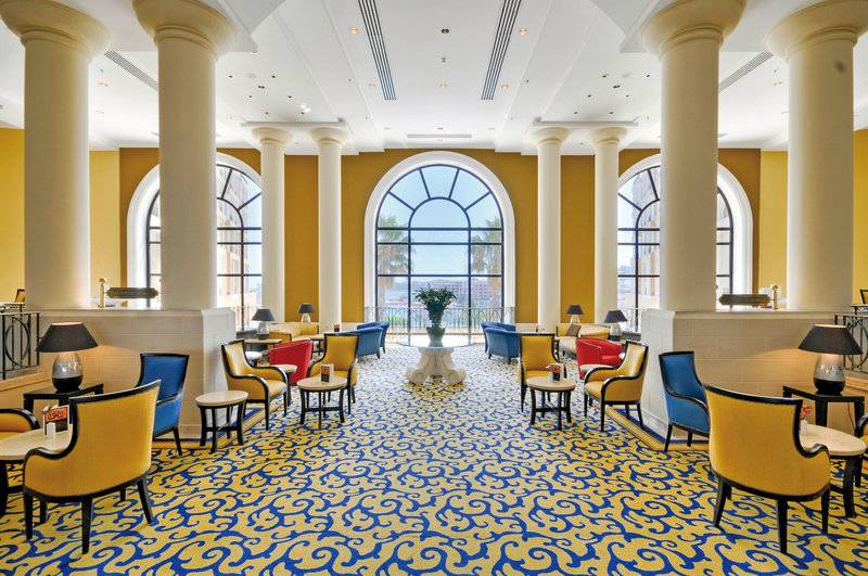 Lobby des Corinthia St. George's Bay Hotels mit gelben und blauen Mustern und großen Fenstern.