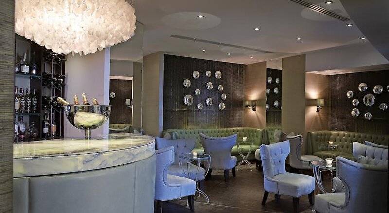 Loungebereich im Corinthia St George's Bay Hotel mit grünen Sofas, weißen Stühlen und einer Theke.