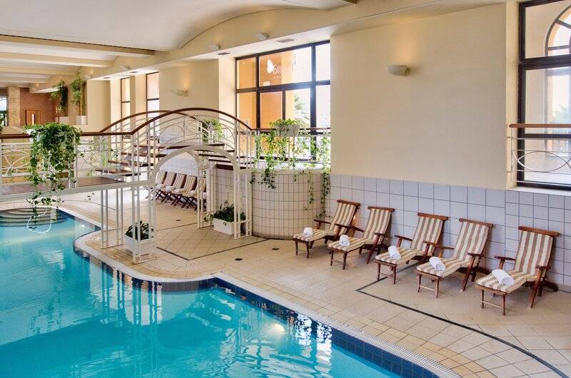 Innenpool im Corinthia St. George's Bay Hotel mit Sonnenliegen und Treppen.