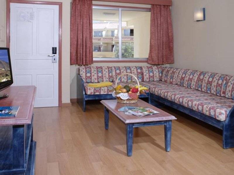Wohnzimmer im Hovima Jardin Caleta Hotel mit Couch, Tisch, Früchtekorb und Fernseher.
