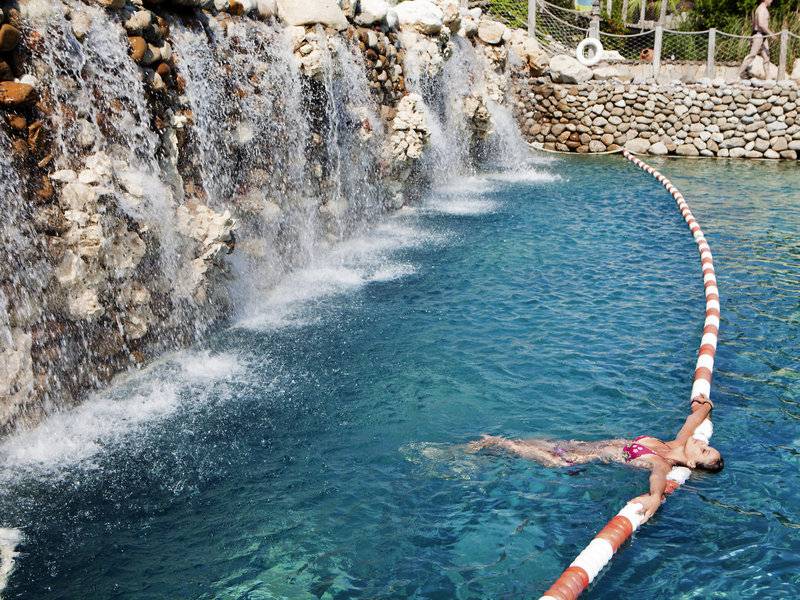 Eine Frau schwimmt im Pool mit einem Wasserfall im Hintergrund.