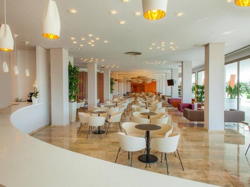 Innenbereich des RH Bayren & Spa Hotels mit vielen Tischen und Stühlen, Pflanzen und hängenden Lampen.