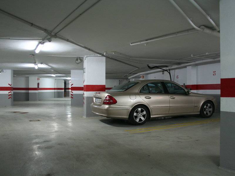 Unterirdischer Parkplatz mit einer beigefarbenen Limousine, gekennzeichnet durch rote und weiße Säulen.