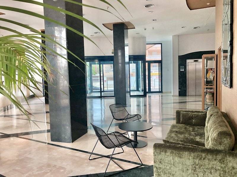 Eingangsbereich eines Hotels mit Sofa und Stühlen vor einer großen Glastür.
