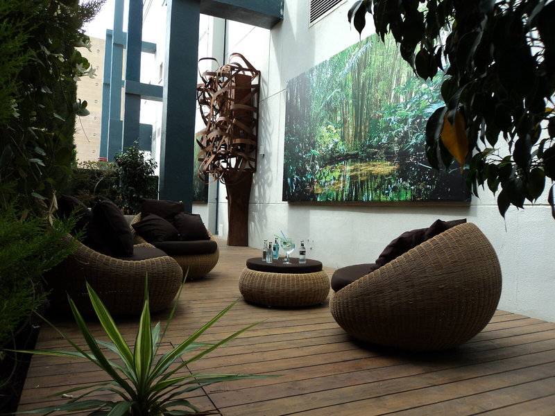 Gartenlounge im Principal Afilliated by RH mit Korbsesseln und einem großen Gemälde an der Wand.