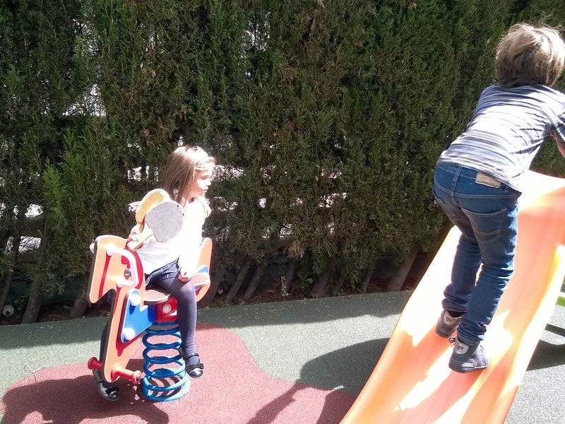 Zwei Kinder spielen auf einem Spielplatz, eines auf einem Pferdchen und das andere auf einer Rutsche.