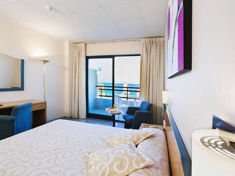 Hotelzimmer mit Meerblick, Bett, Schreibtisch und zwei Stühlen.
