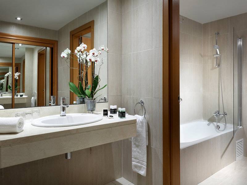 Badezimmer im Hotel Exe Rey Don Jaime mit Waschbecken, Spiegel, Badewanne und Orchideen.