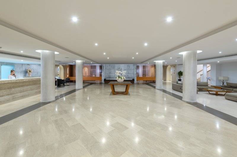 Empfangshalle des Lindos Royal Resorts mit weißem Boden, hohen Säulen und eingeschalteten Deckenleuchten.