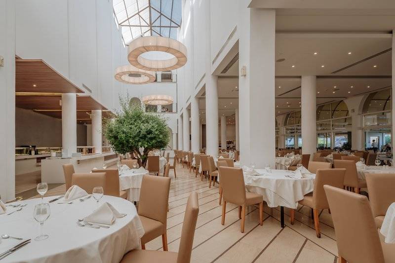 Innenansicht des Restaurants im Lindos Royal Resort mit runden Kronleuchtern und eleganten Esstischen.