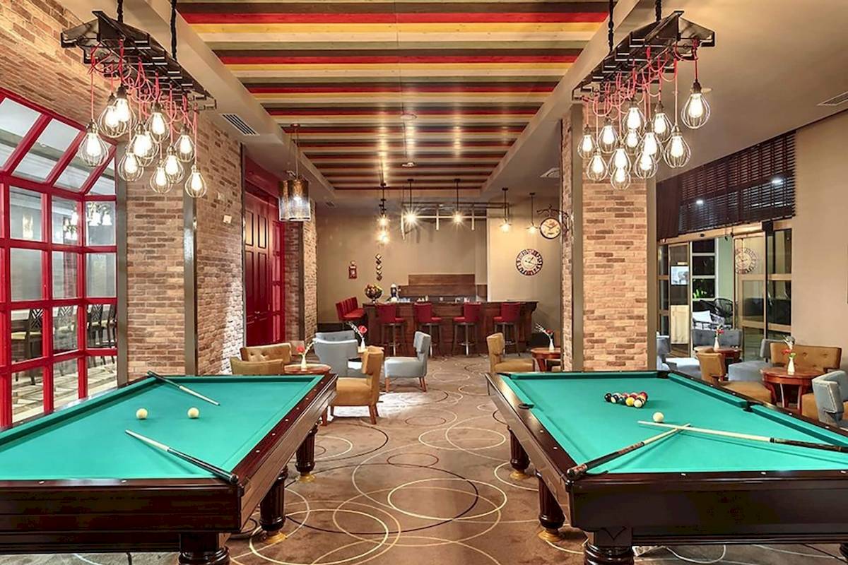 Zwei Pooltische in der Lobby des Sunis Efes Royal Palace Resort & Spa mit farbigen Deckenleuchten und roten Fenstern.