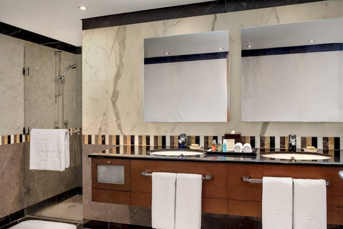 Ein Badezimmer im Al Ain Rotana Hotel mit einer Dusche, zwei Waschbecken und Spiegeln.