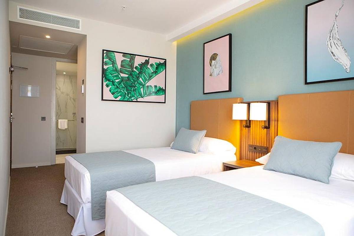 Doppelzimmer im Riu Plaza Espana Hotel mit zwei Betten, Nachttischen und Kunstwerken an der Wand.