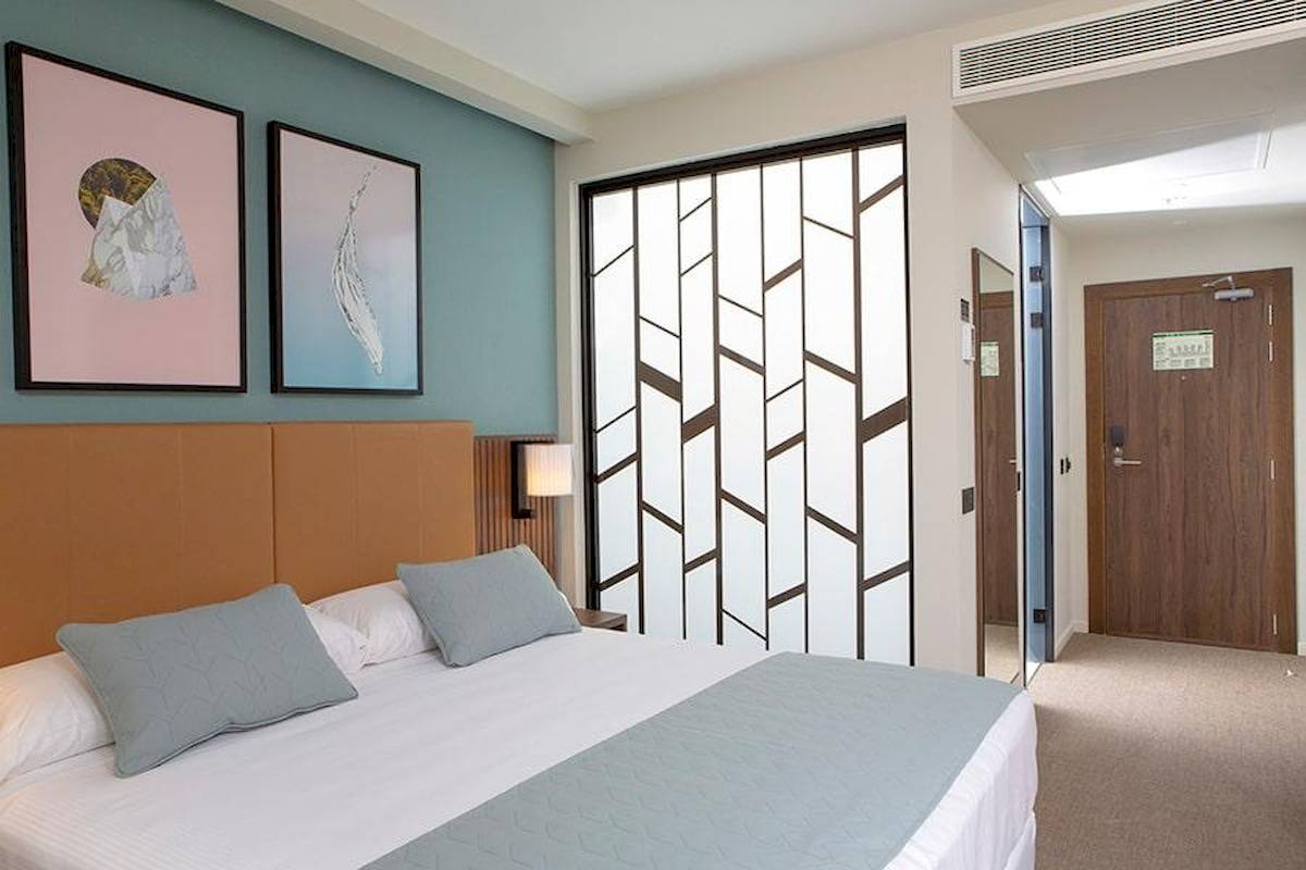 Hotelzimmer im Riu Plaza Espana mit Bett, Kissen, Kunstwerken an der Wand und einer Schiebetür.