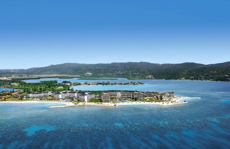 Luftaufnahme des Secrets St. James Hotel am Strand mit blauem Wasser und Bergen im Hintergrund