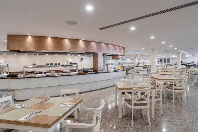 Innenansicht des Restaurants im ALUA Gran Camp de Mar Hotel mit einer langen Theke und runden Tischen.
