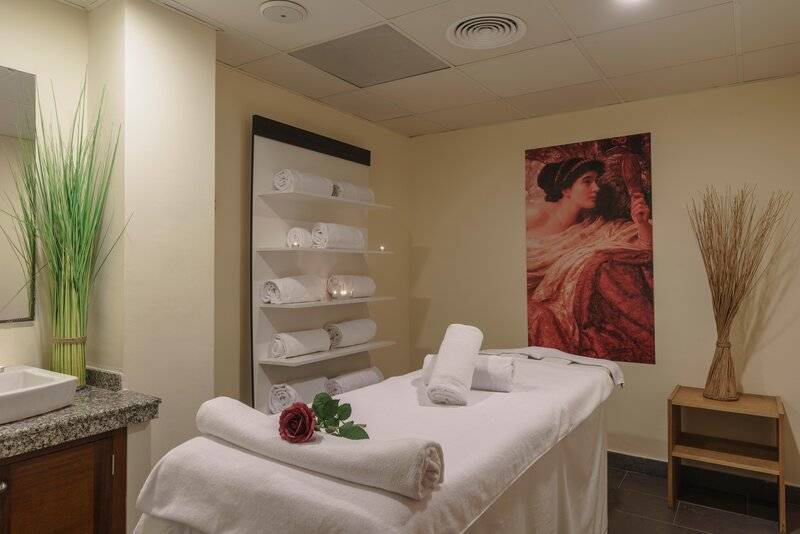 Spa-Behandlungsraum im ALUA Gran Camp de Mar mit Massageliege, Toilettenartikeln und Wanddekoration.