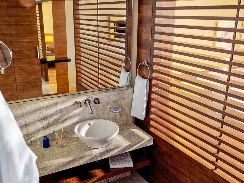 Badezimmer im TUI BLUE Side Hotel mit Waschbecken, Spiegel und Holzjalousien.