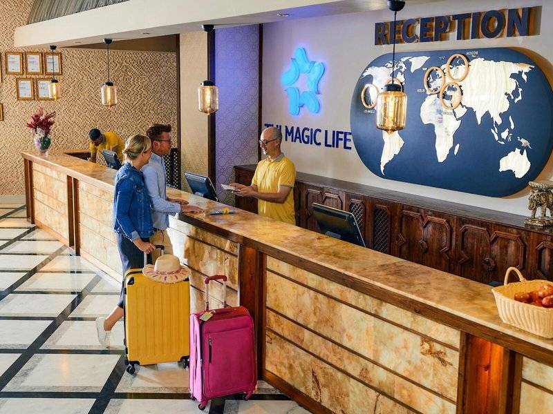 Rezeption im Magic Life Jacaranda Hotel mit Mitarbeitern und Gästen, die Gepäck haben.