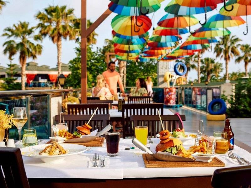 Terrasse im Magic Life Jacaranda Hotel mit bunten Regenschirmen, bunten Tischen und Stühlen, Essen und Getränken.