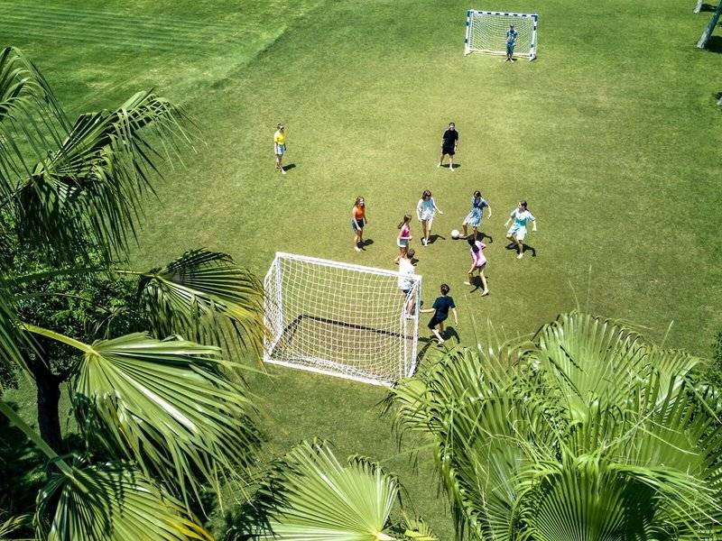 Kinder spielen Fußball auf einem grünen Rasenfeld im Magic Life Jacaranda Hotel.
