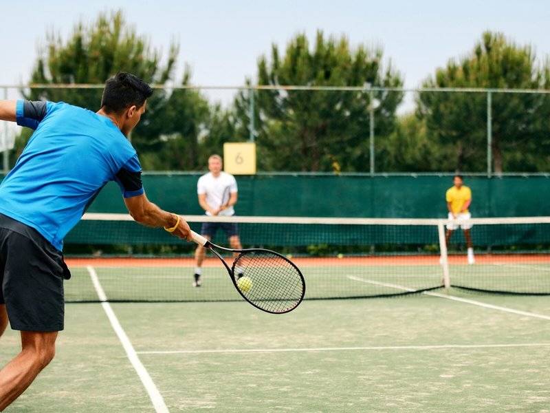 Tennisspieler im Magic Life Jacaranda schlagen den Ball über das Netz.