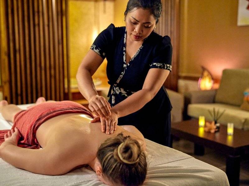 Eine Frau erhält eine Massage in einem Hotel, während eine Therapeutin sie massiert.