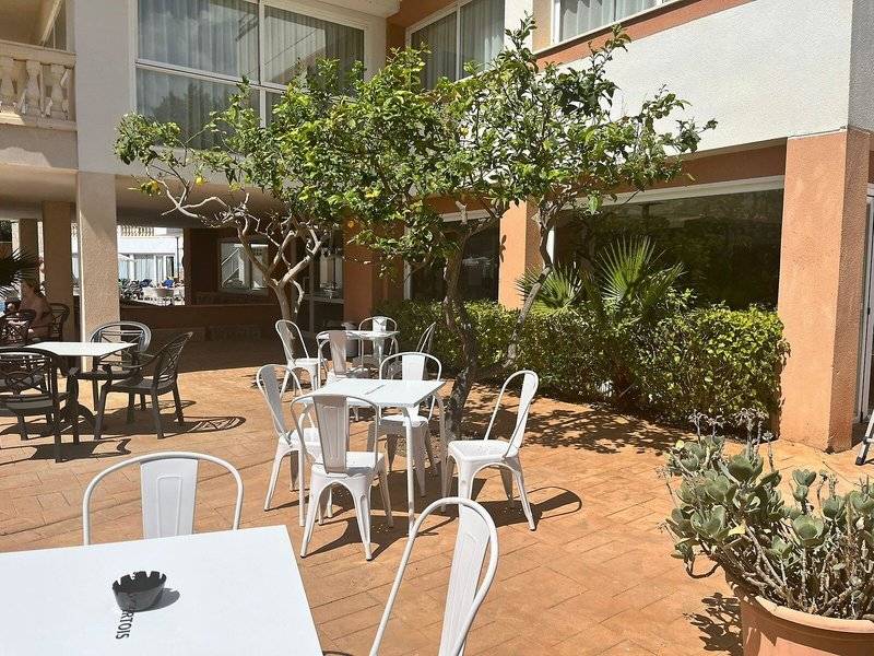 Außenterrasse des Canyamel Classic Hotels mit weißen Tischen und Stühlen, umgeben von Pflanzen und Bäumen.