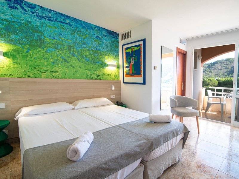 Hotelzimmer im Canyamel Classic mit Doppelbett, Kunstwerk an der Wand und Balkonzugang.