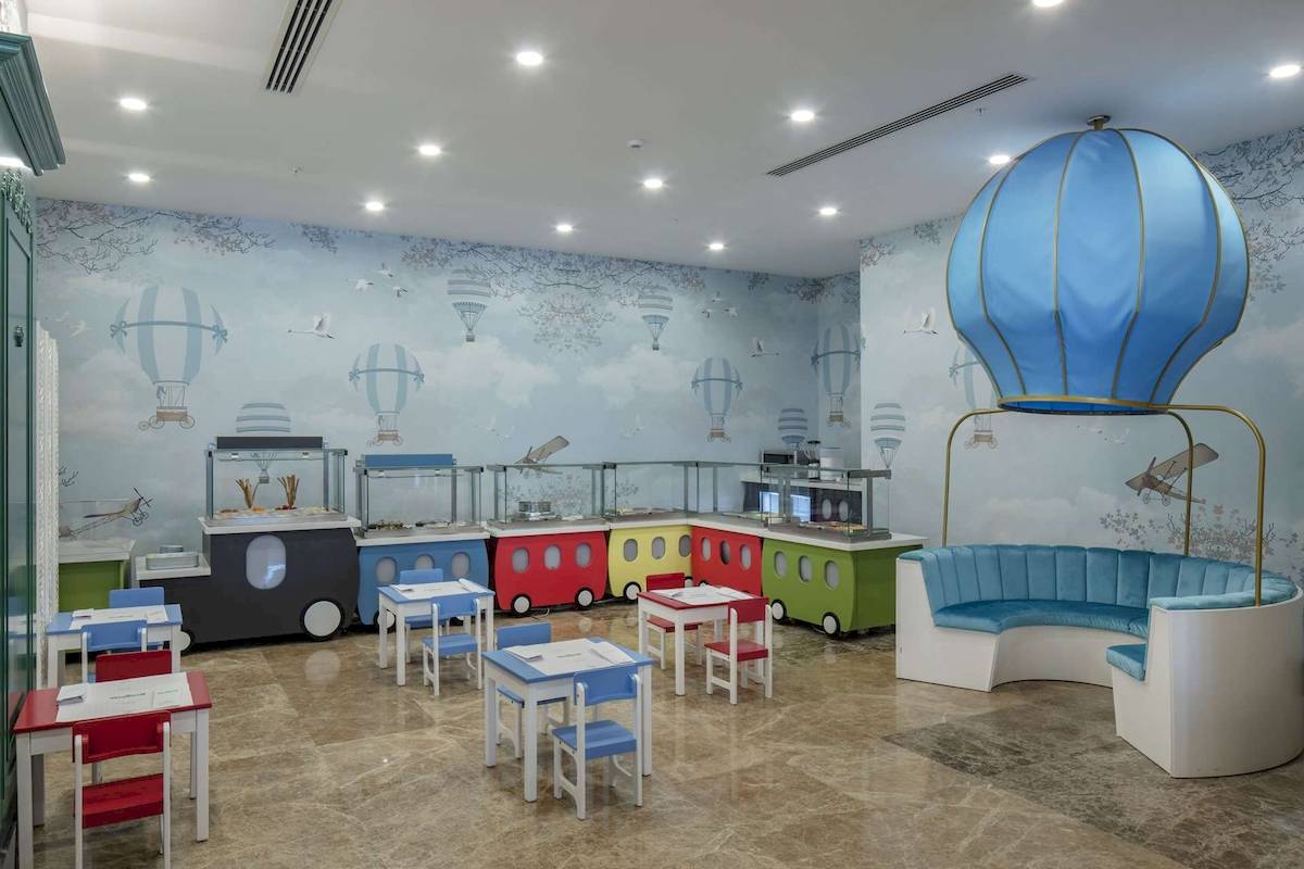 Kinderfreundliches Esszimmer im Hotel Granada Luxury Okurcalar mit bunten Wagen und Heißluftballon-Wanddekoration.