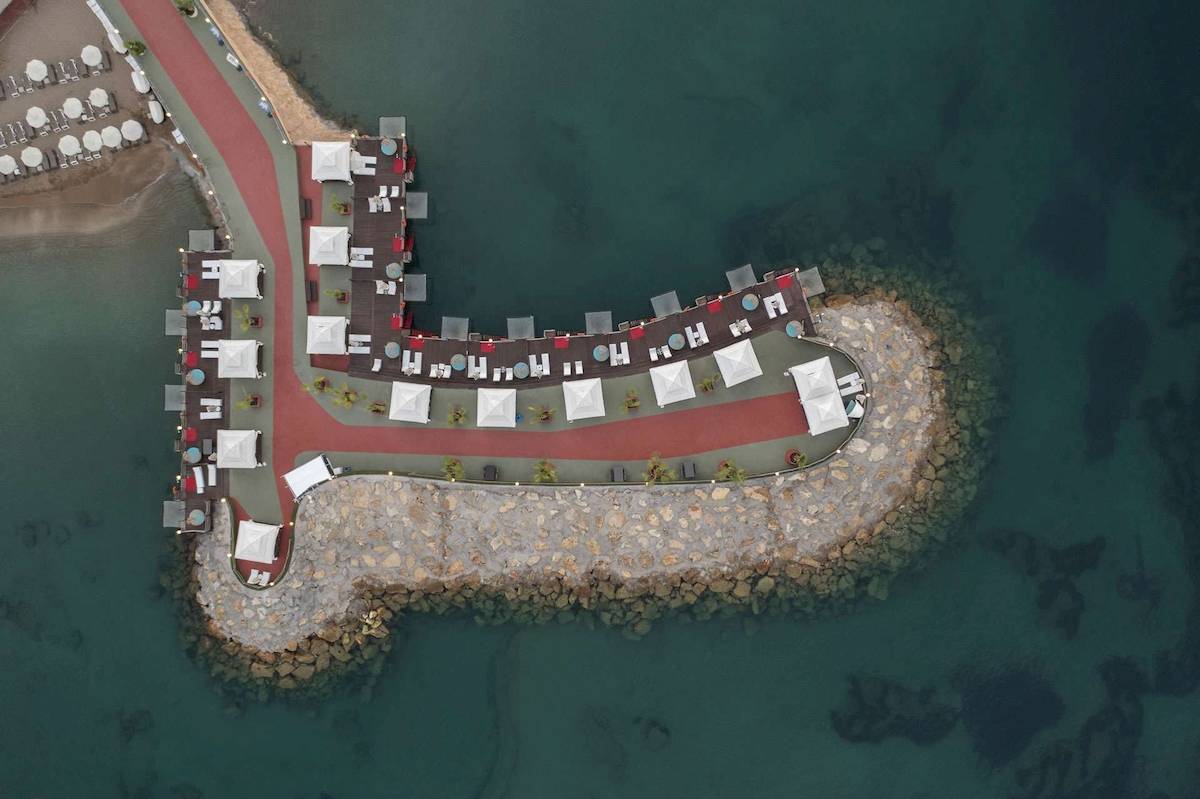 Luftaufnahme des Granada Luxury Okurcalar Hotels am Strand mit weißen Sonnenschirmen und roten Wegen.