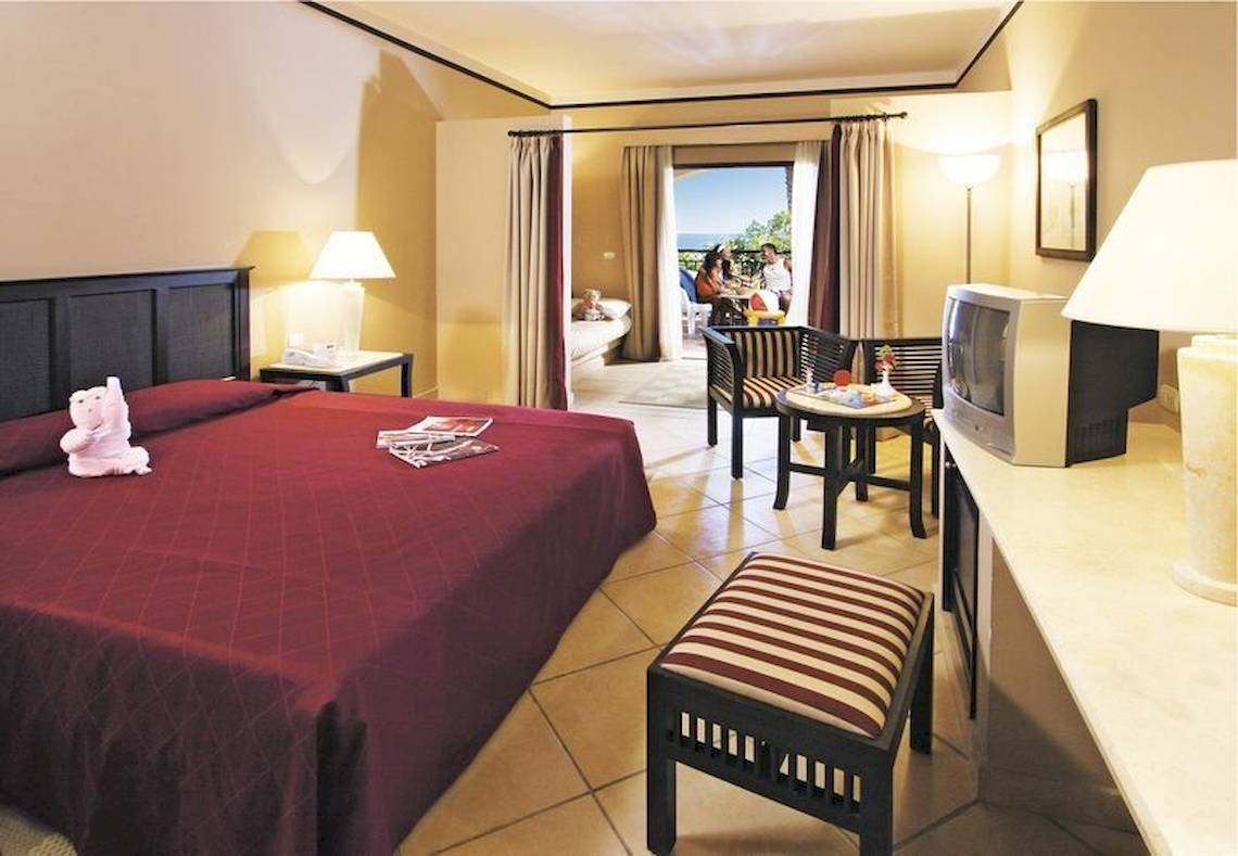 Innenansicht eines Hotelzimmers im Jaz Belvedere Resort mit einem Doppelbett, Möbeln und Aussicht auf den Balkon.