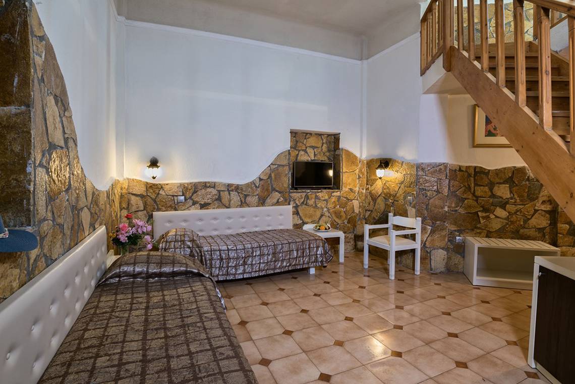 Doppelzimmer im Eliros Mare Hotel mit Steinwänden, zwei Betten, Fernseher und Holztreppe.