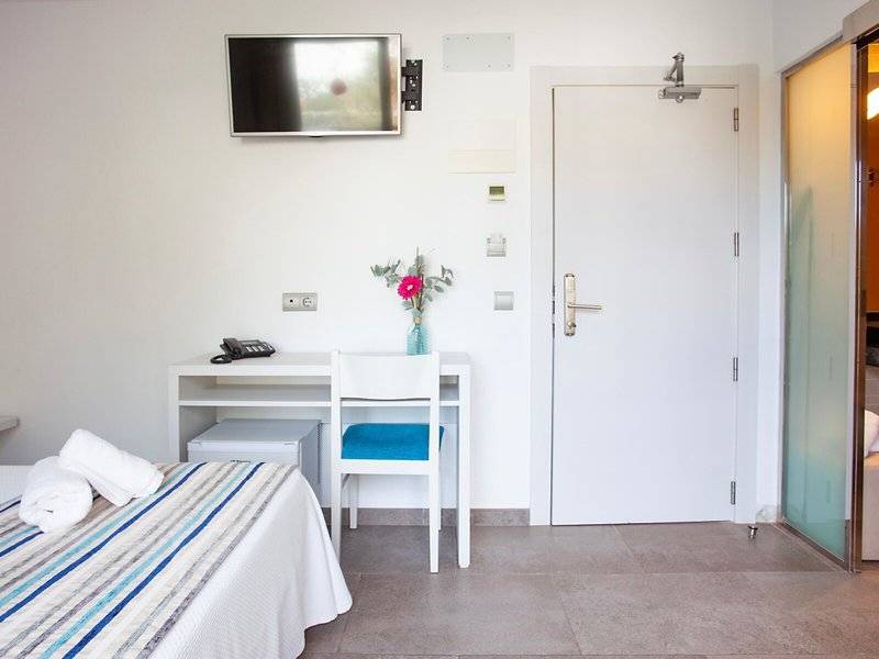 Innenansicht eines Hotelzimmers von Rosales Formentera mit Bett, Schreibtisch und Fernseher an der Wand.