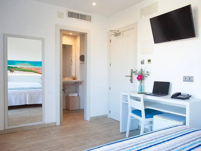 Innenansicht eines Hotelzimmers von Rosales Formentera, mit Schreibtisch, Laptop, Telefon und Fernseher.