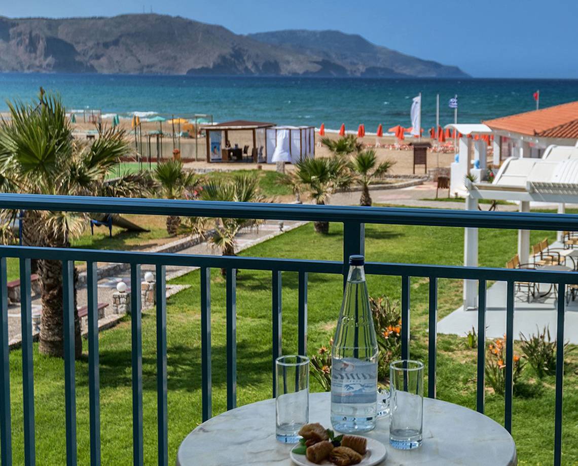 Aussicht auf den Strand im Eliros Mare Hotel mit Tisch, Wasserflasche und Gebäck.