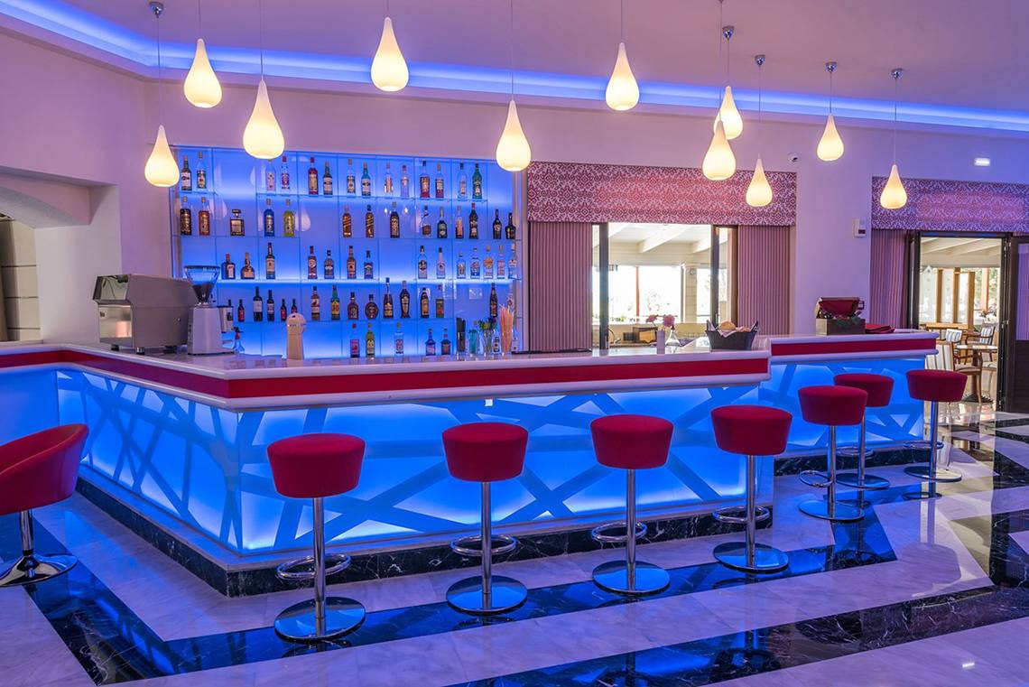 Die Bar im Eliros Mare Hotel mit blauen Beleuchtung und roten Stühlen.