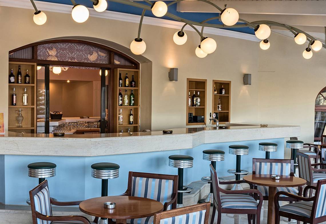 Innenansicht der Bar im Eliros Mare Hotel mit Tresen, Stühlen und Flaschen.