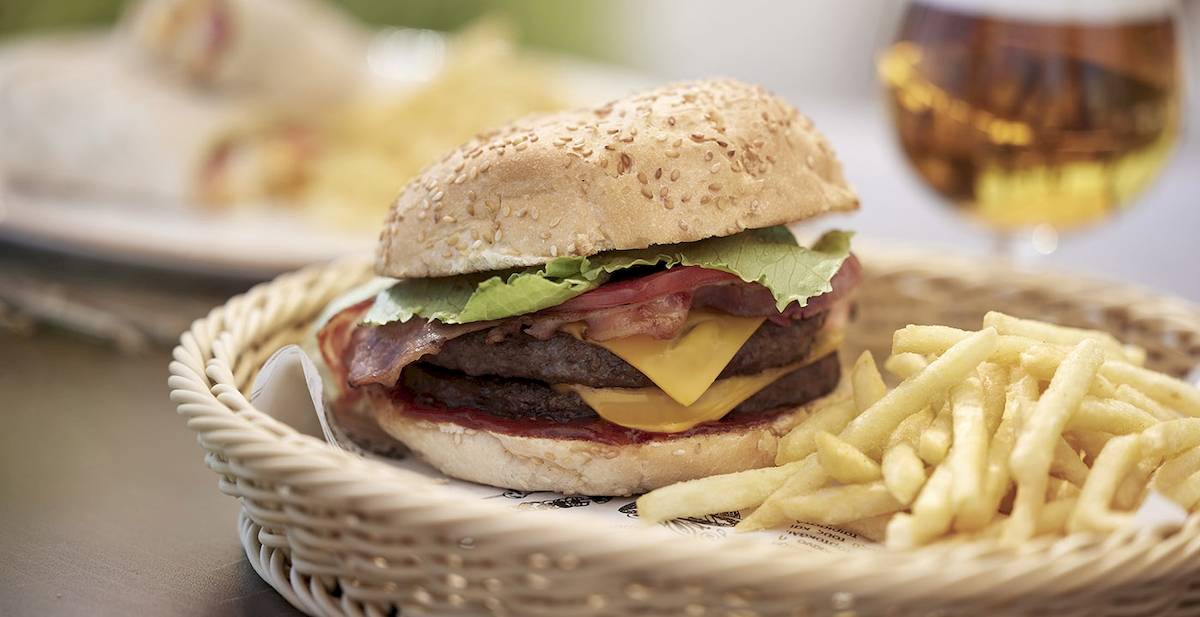 Ein Burger mit Pommes in einem Korb auf einem Tisch neben einem Glas Bier.