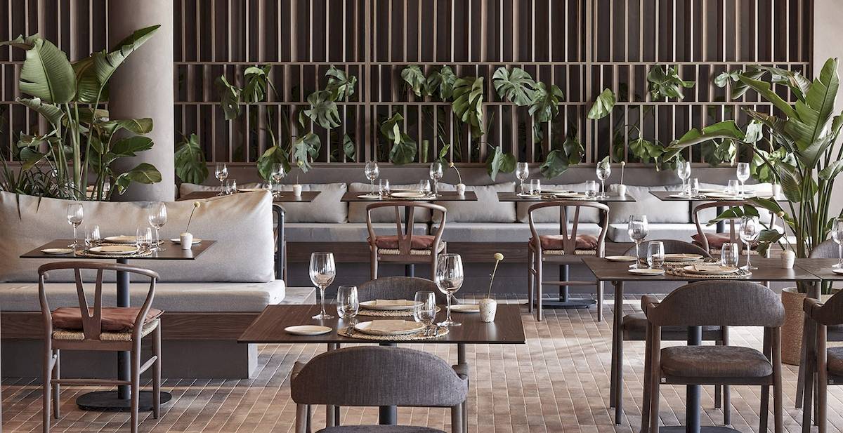 Innenansicht des Restaurants im Helea Lifestyle Beach Resort mit gedeckten Tischen und grünen Pflanzen.