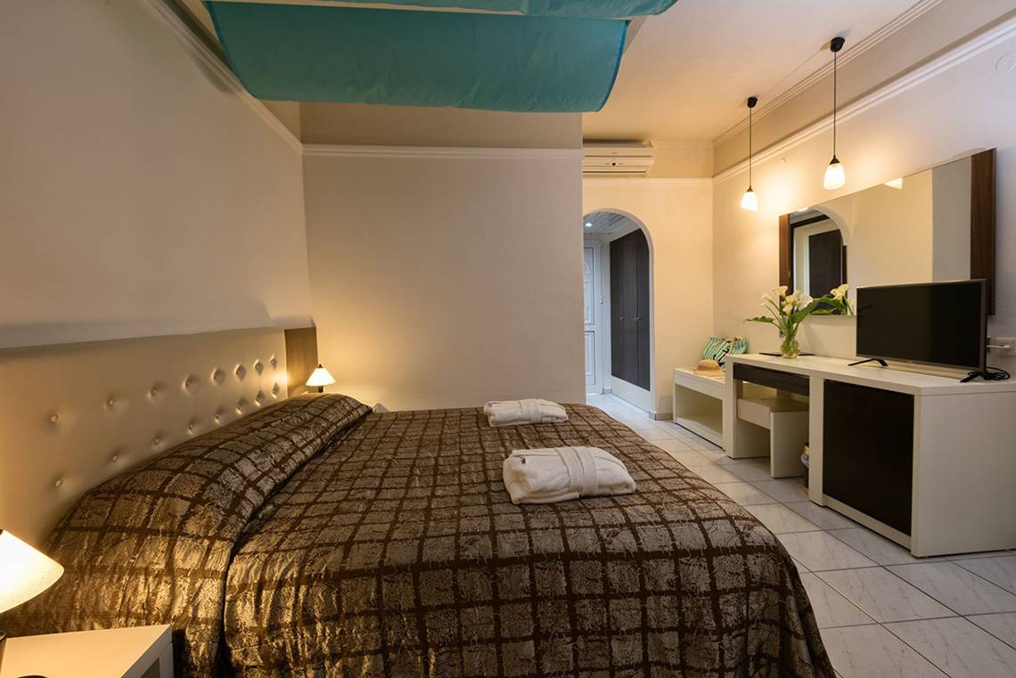 Schlafzimmer im Eliros Mare Hotel mit Bett, Fernseher, Spiegel und Dekor.