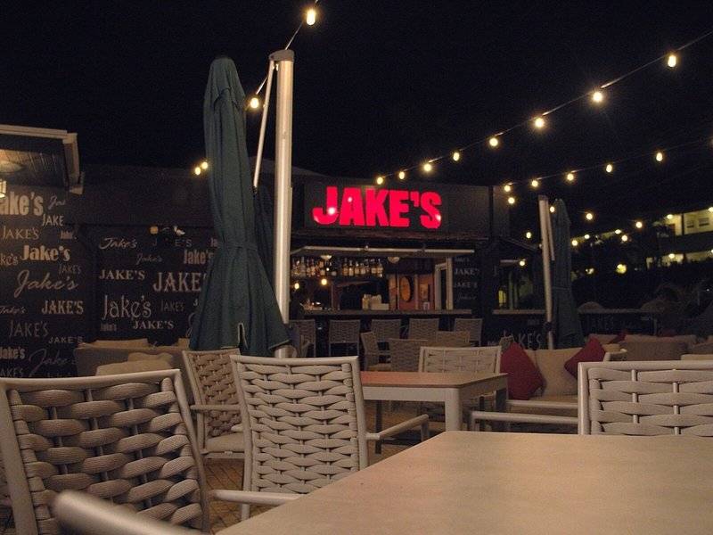 Nachtansicht der Terrasse von Jake's im Coconut Court Beach Hotel mit leuchtenden Lichtern und Tischen.