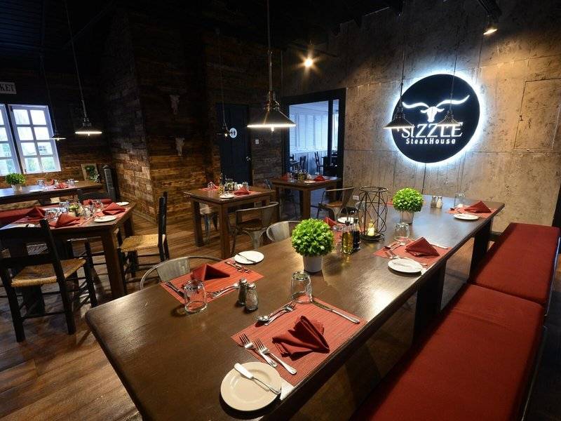 Inneneinrichtung des Sizzle Steakhouse mit langen Holztischen, roten Sitzbänken und grün dekorierten Tischen.