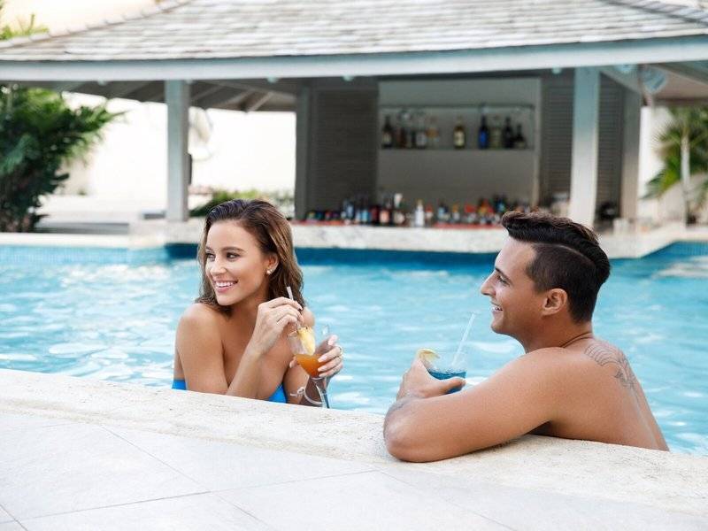 Zwei Leute am Pool im Sugar Bay Barbados, die Cocktails trinken und lächeln.