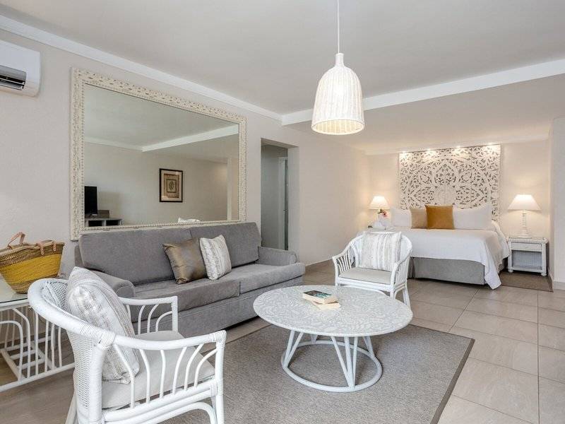 Modernes Zimmer im Sugar Bay Barbados Hotel mit grauem Sofa, weißem Tisch und großem Spiegel.