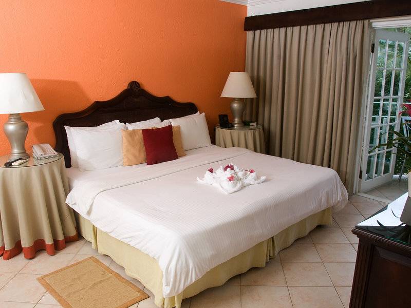 Schlafzimmer im Mango Bay Hotel mit zwei Nachttischen, Lampen und einem großen Bett, das mit weißen Laken und bunten Kissen ausgestattet ist.