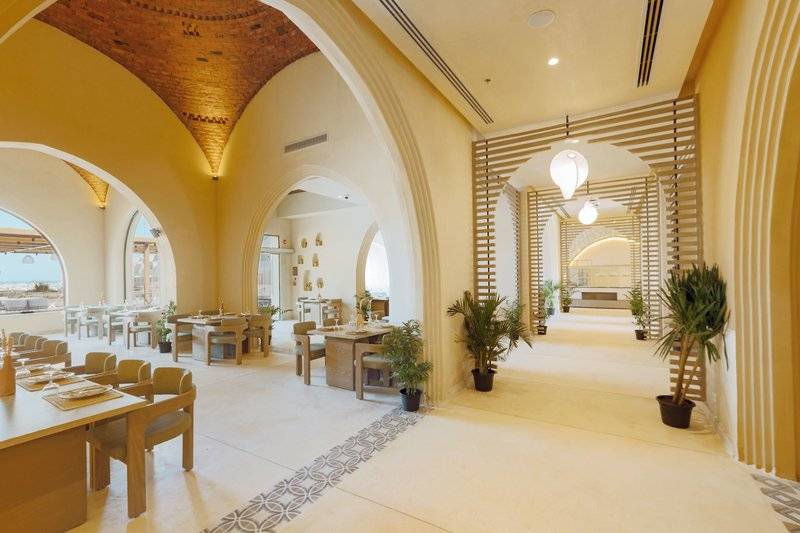 Innenbereich des Sunrise Anjum Resort Restaurants mit gelben Wänden, Holztischen, Stühlen und Pflanzen.