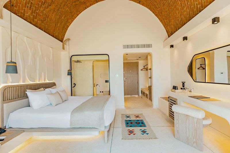 Innenansicht eines eleganten Zimmers im Sunrise Anjum Resort mit einem großen Bett, weißen Wänden und einem großen Spiegel.