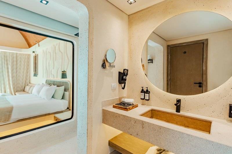 Innenansicht des Badezimmers im Sunrise Anjum Resort Hotel mit Spiegel, Waschbecken und Bett im Hintergrund.