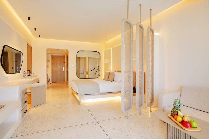 Interieur eines eleganten Zimmers im Sunrise Anjum Resort mit einem Bett, Spiegeln und Obst auf einem Tisch.